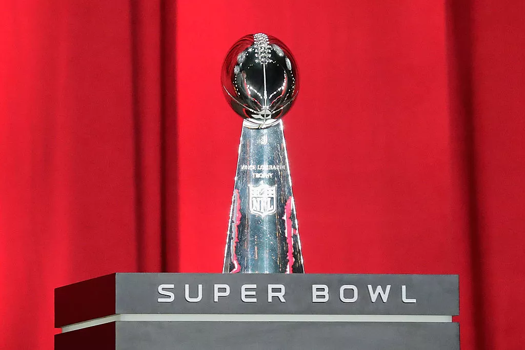 Super Bowl Lombardi Trophy on display with red curtains in background.