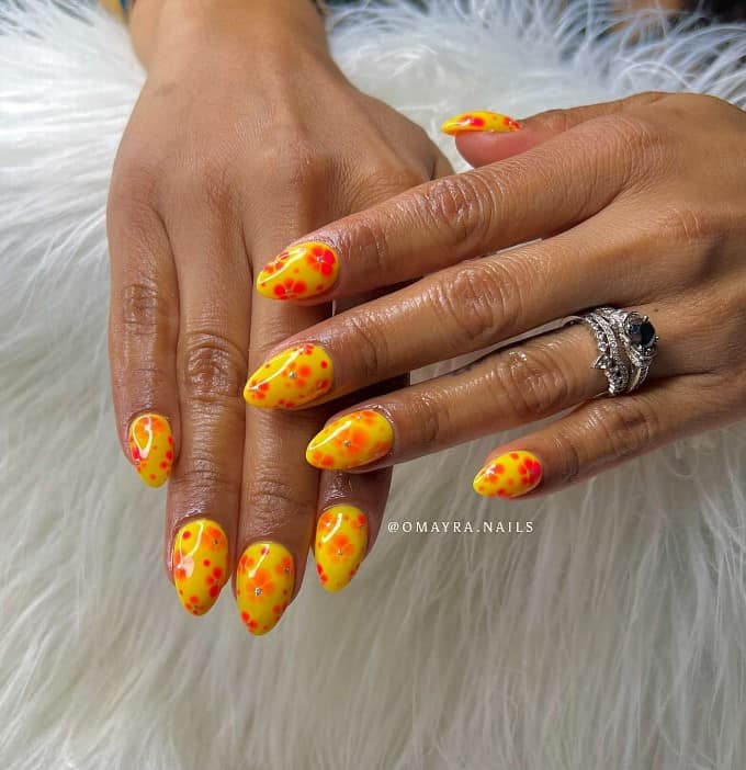 A woman's almond shaped nails with bright yellow nails that has orange flowers nail designs