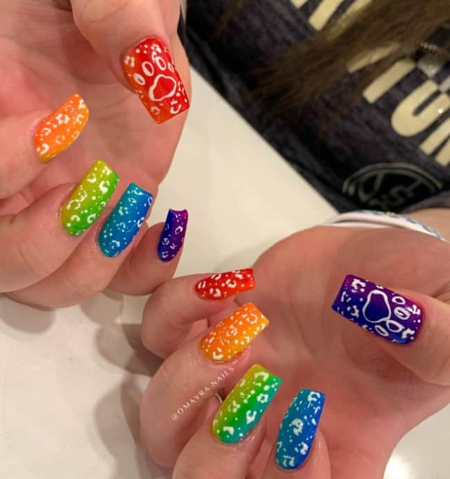 A woman's long nails with rainbow ombre nails that has white ink blots and paws nail designs