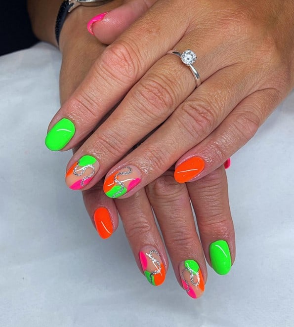 A woman's short nails with nude peach, neon green, pink, and orange nail polish that has irregularly shaped circles in the same shades with silver swirls nail designs