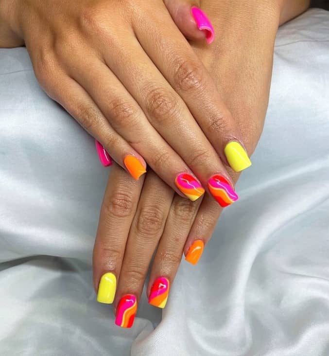 A woman's nails with bright pink, orange, and yellow nail polish that has swirls of the same colors on accent nails