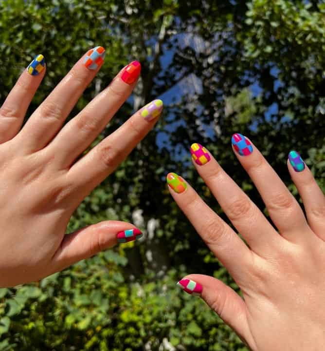 A closeup of a woman's fingernails with multicolored checkered patterns that has color combinations like pink and yellow and blue and red