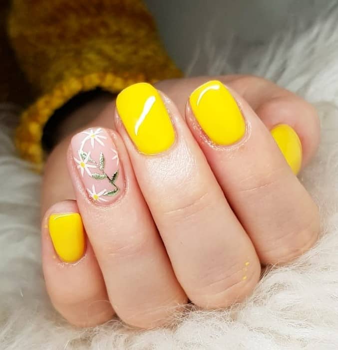 A closeup of a woman's short nails with nude and yellow nail polish base that has daisies and a lone shimmering green leaf stem on nude nails