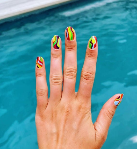 A woman's short nails with sharp swirls and streaks of assorted bright and dark colors