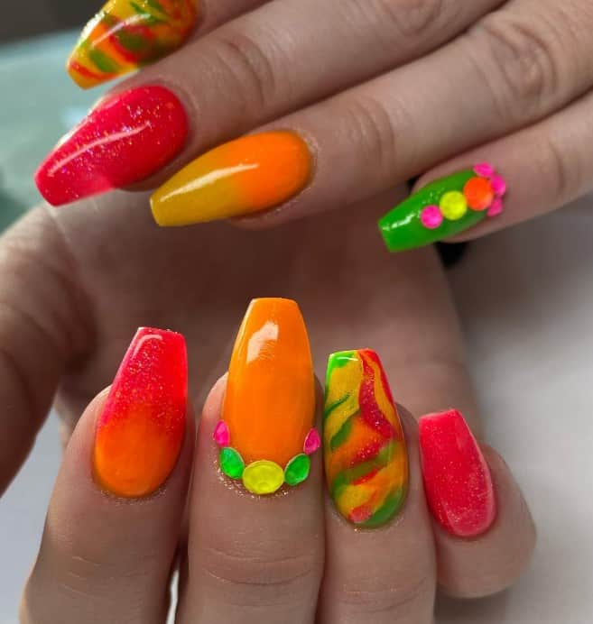 A closeup of a woman's long coffin nails with mix of bright colors like bright orange, sunny yellow, green, and red nail polish in glittery finish