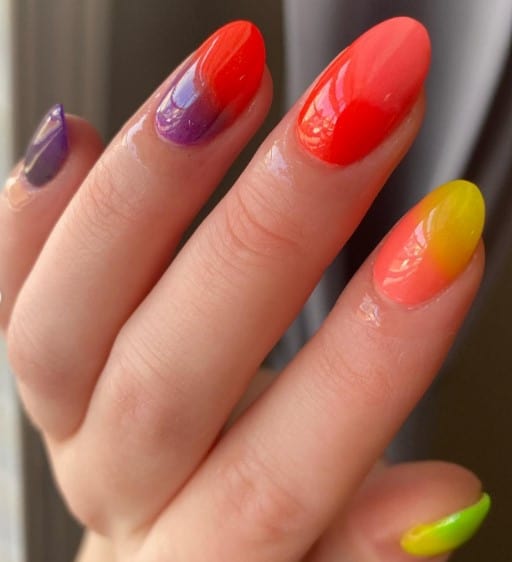 A closeup of a woman's oval shaped nails with bright nail design in a unique ombre effect