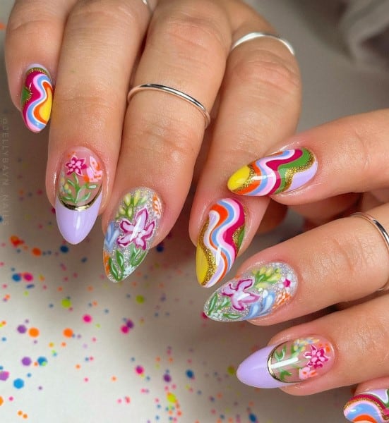 A closeup of a woman's long almond nails with multi-colored swirls, delicately hand-painted florals, and gold-outlined lavender French tips