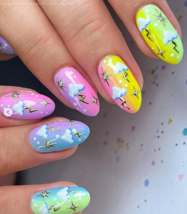 A closeup of a woman's long oval nails with gradients of blue, green, purple, pink, and yellow hues that has fluffy clouds, golden lightning zaps, and twinkling stars in silver nail designs