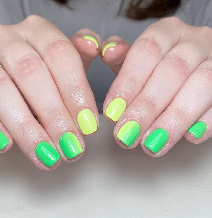 A closeup of a woman's short nails with a mix of green and yellow hues in an ombre effect