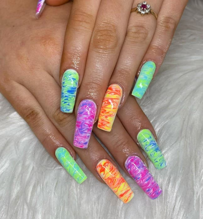 A closeup of a woman's long square nails with two vibrant hues that are blended creating long swirls in a watercolor effect