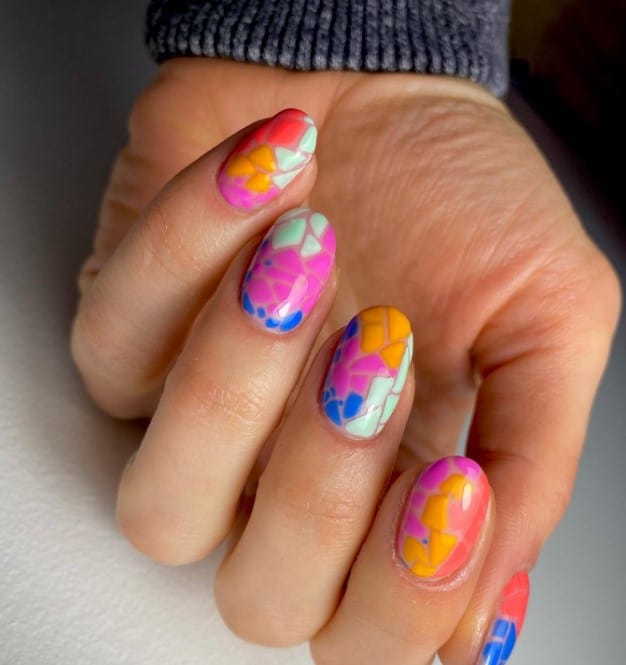 A closeup of a woman's mid-length nails with trio of striking colors that has cracked eggshells nail designs