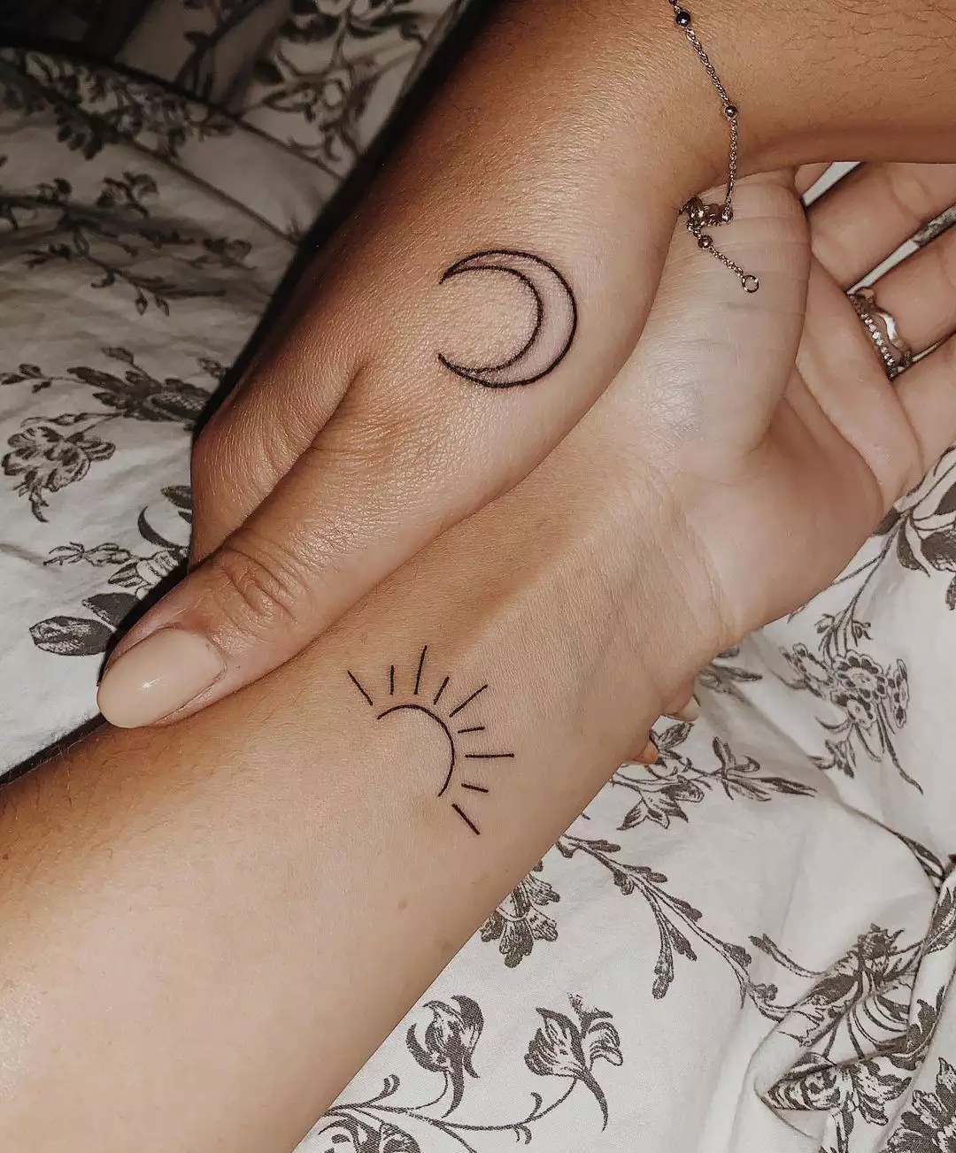 Close up of two hands, one with a sun tattoo and one with a moon