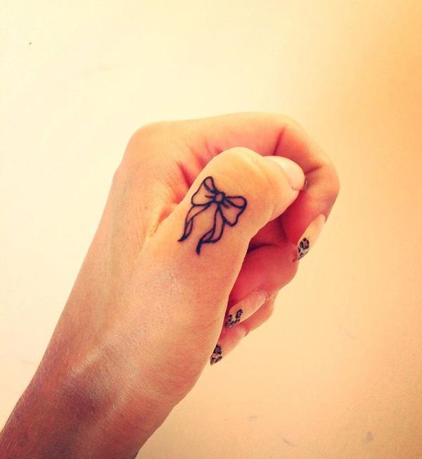 A Bow outline tattoo on thumb finger