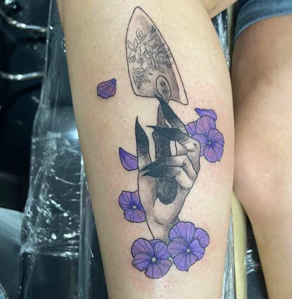 A hand holding a shovel surrounded with violet flowers