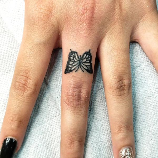 Black butterfly tattoo on middle finger