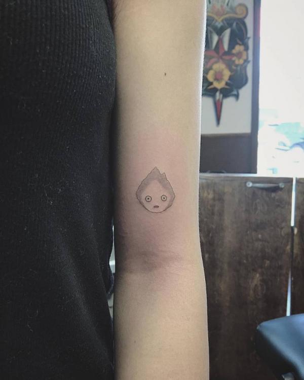 Dainty Calcifer tattoo above inner elbow