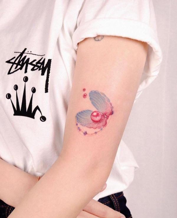 Feminine shell with pearls tattoo on upper arm