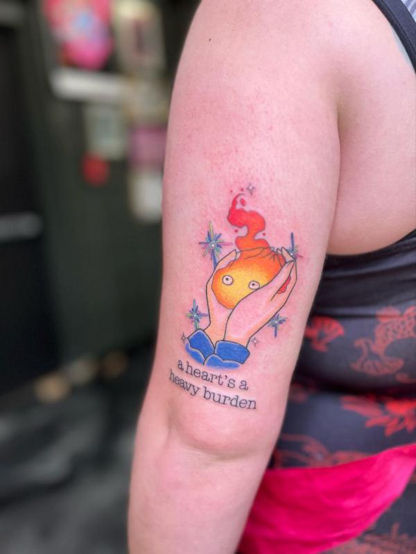 Hands holding Calcifer tattoo with quote A heart is heavy burden