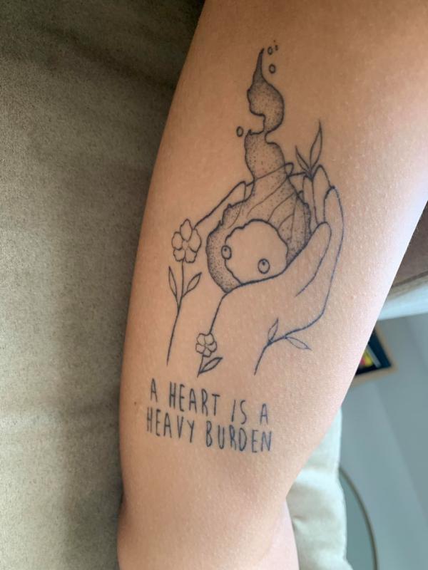 Hands holding Calcifer upper arm tattoo