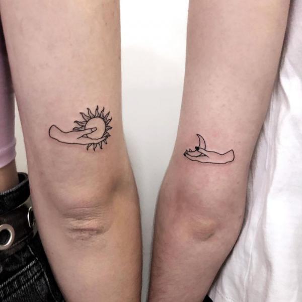 Hands holding sun and moon matching tattoo above elbow