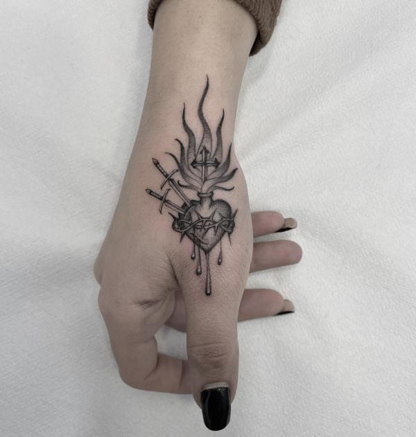 Sacred heart with daggers tattoo on top of thumb finger