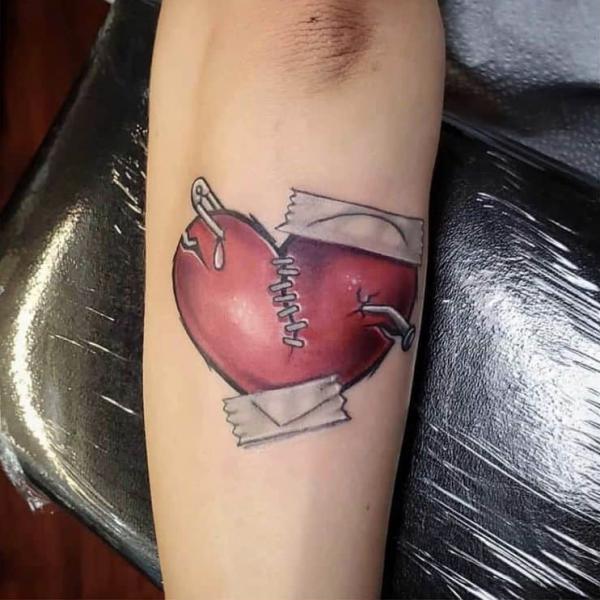 Stitched broken heart with bandage and safety pin tattoo on forearm