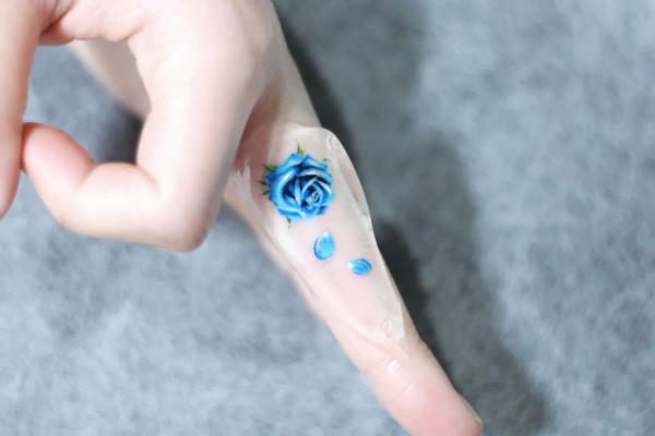 Tiny blue rose finger tattoo