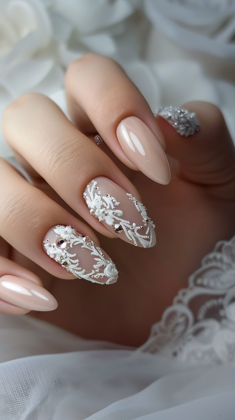 Almond-shaped nails with a sheer nude base, adorned with white intricate lace patterns and delicate crystals, perfect for a bridal look.