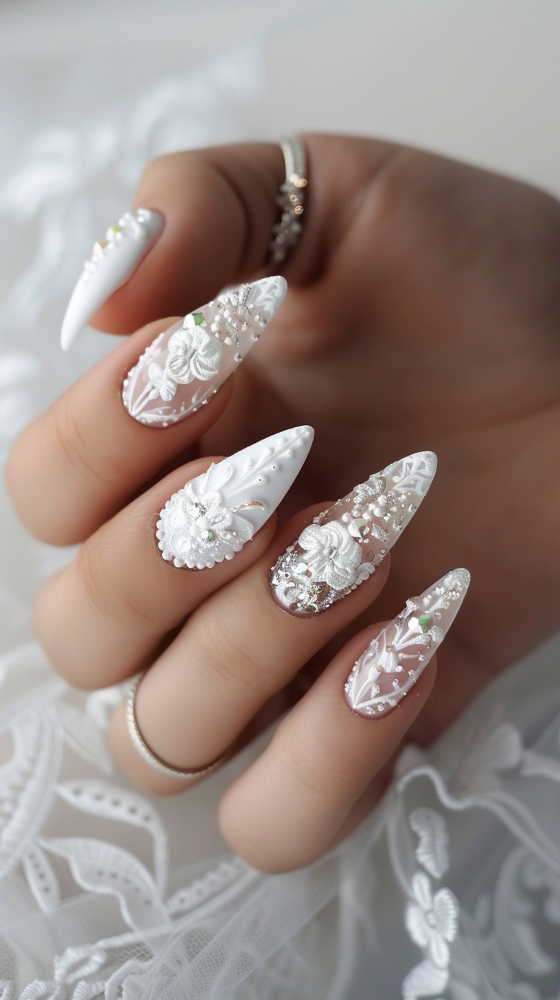 Stiletto nails with a nude base, featuring raised white floral 3D art, accented with pearls and delicate crystal embellishments for a luxurious bridal design.