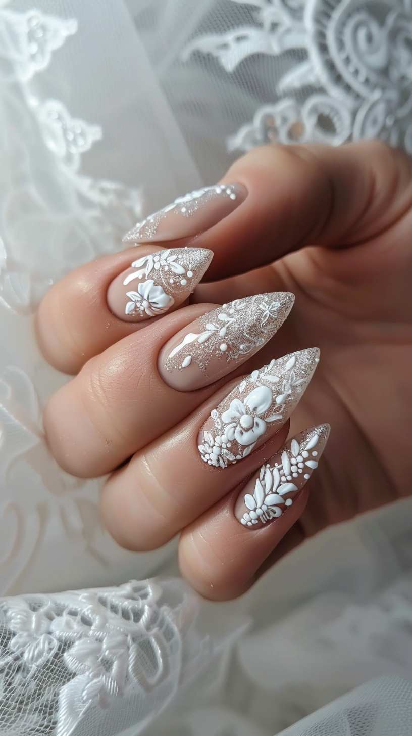 The bridal nails feature a stunning white floral design against a neutral base, with intricate 3D flower appliques, shimmering glitter, and delicate pearl accents. The almond-shaped nails provide an elegant canvas for the detailed lace-like patterns and sparkling embellishments, creating a romantic and luxurious look fit for a wedding day.