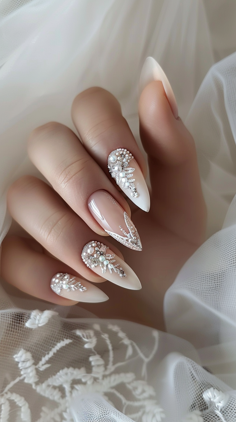 The image shows elegantly designed bridal nails with a nude base color and intricate white and silver embellishments. The nails feature pearls, crystals, and delicate floral or feather-like patterns carefully arranged to create a glamorous and romantic look befitting a wedding. The stiletto or pointed nail shape adds to the sophisticated, feminine style.