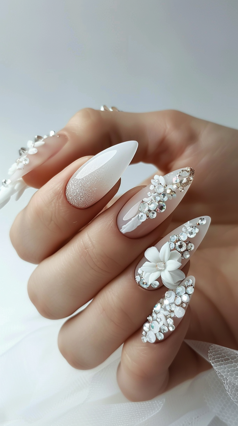 The nails feature a soft white base with one nail adorned with an ombre rose gold glitter accent. The showstopping elements are the intricate clusters of pearls, crystals, and a delicate 3D floral embellishment that gracefully trail across a few nails, creating a romantic, vintage-inspired look.
