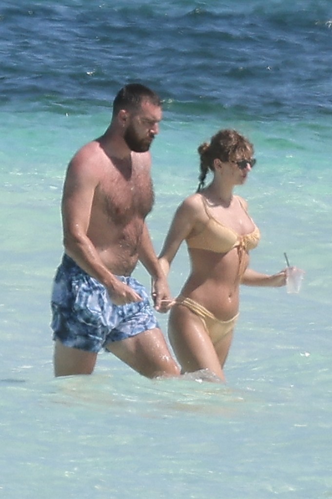 Taylor Swift and Travis Kelce walking on the beach together.