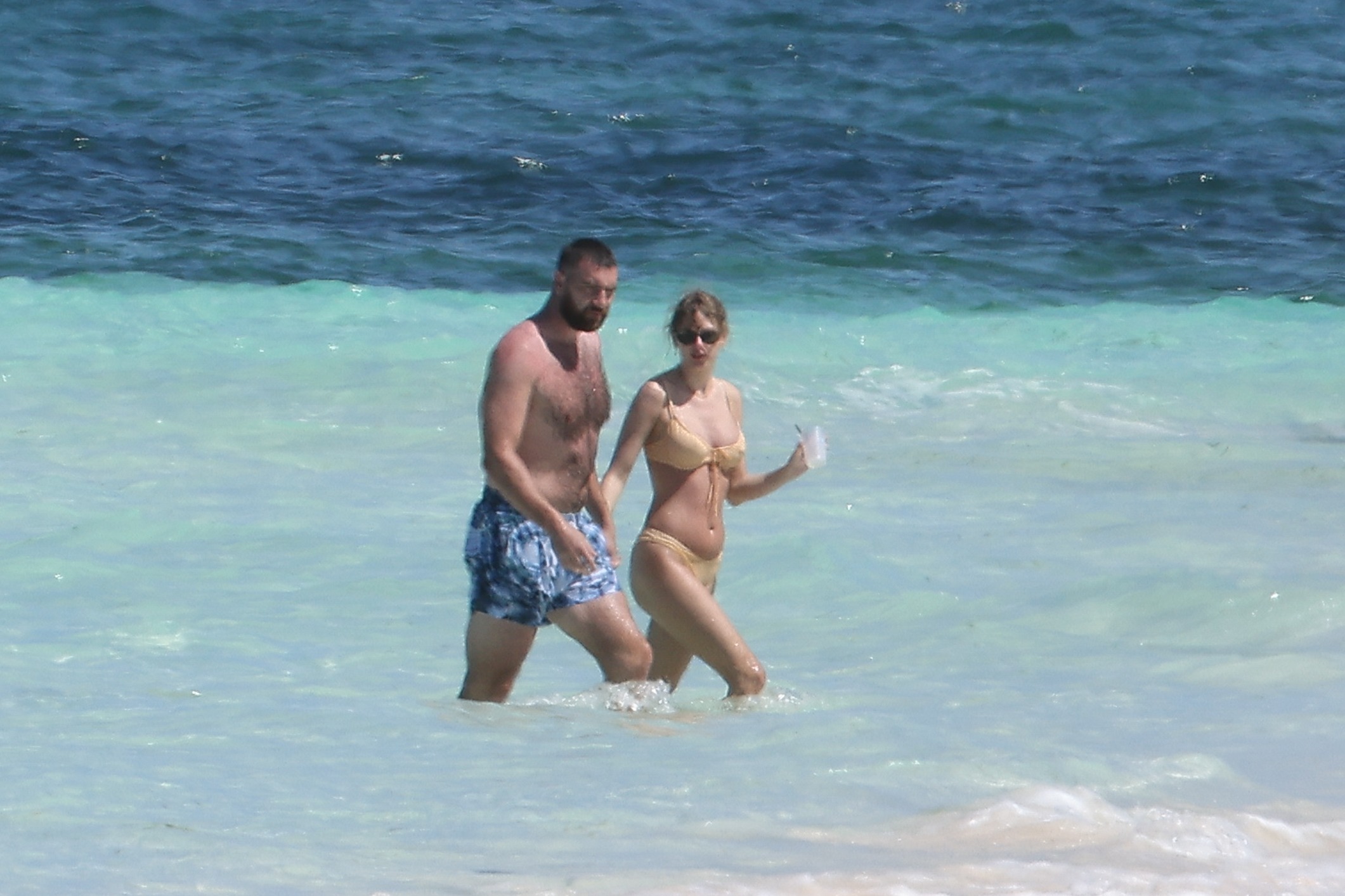 Travis Kelce and Taylor Swift holding hands in the ocean