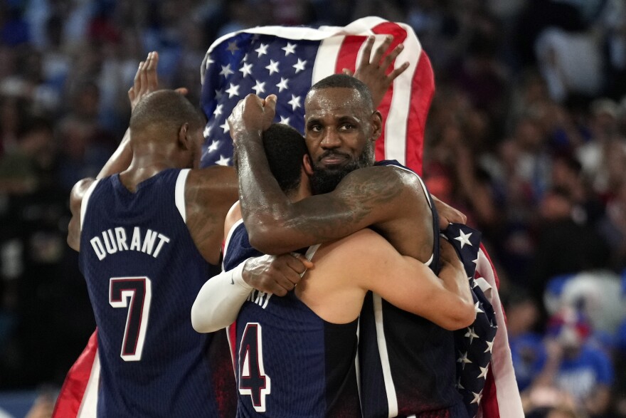 United States' Stephen Curry, center, hugs United States' LeBron James, right, as United States' Kevin Durant hold up an American flag after the United States won a men's gold medal basketball game at Bercy Arena at the 2024 Summer Olympics, Saturday, Aug. 10, 2024, in Paris, France.